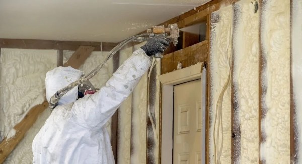 spray foam insulation installed with hose by a worker wearing protection gear